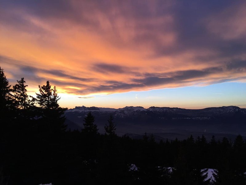 Mountainous landscape at dusk, with dark trees and mountain contours, and a bright sky with orange clouds.jpg